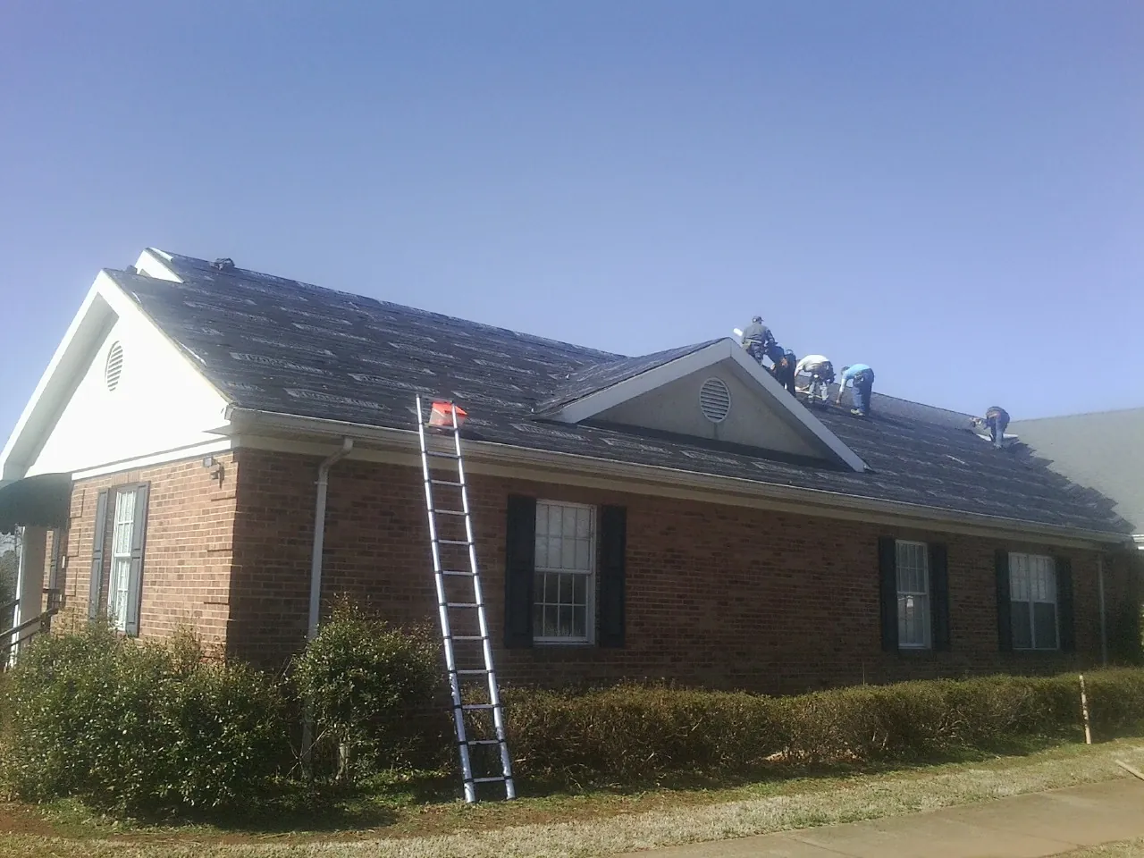 Crew tearing shingles off a brick ranch roof with a ladder set — Metal Roof Repair work by our crew in Pulaski