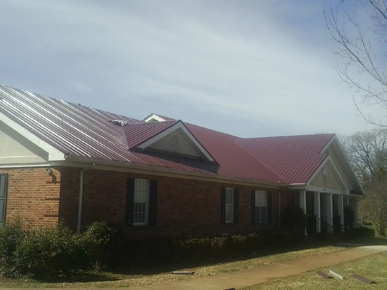 Red metal roof with gabled entries on a long brick building, from a Hail Damage Roof Repair job in Pulaski